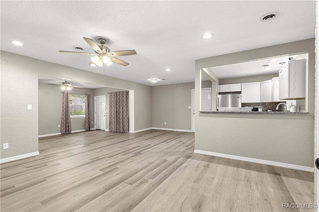 unfurnished living room featuring a textured ceiling, light hardwood / wood-style floors, ceiling fan, and sink