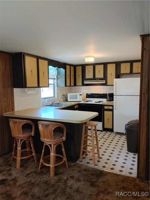 kitchen featuring white appliances, backsplash, a peninsula, under cabinet range hood, and a sink