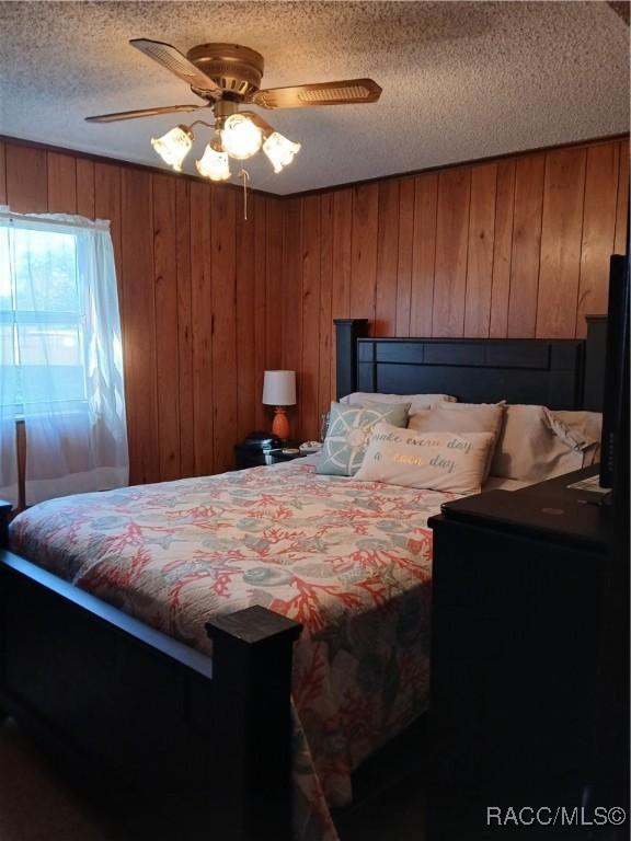 bedroom featuring wood walls, a textured ceiling, and ceiling fan