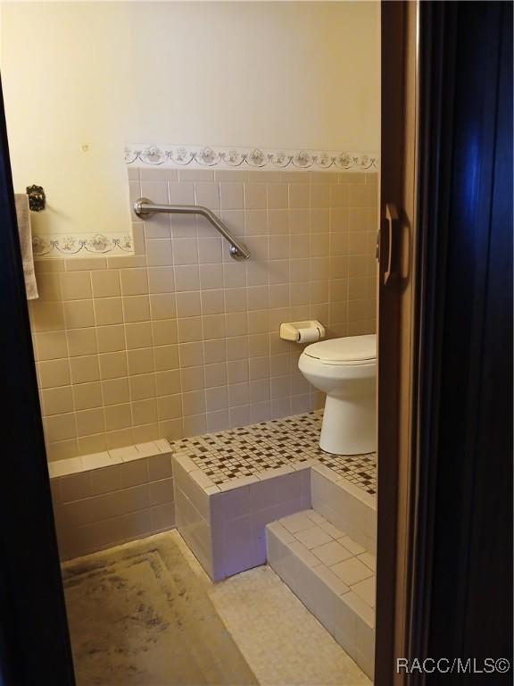 bathroom with tiled shower, wainscoting, tile patterned flooring, and tile walls