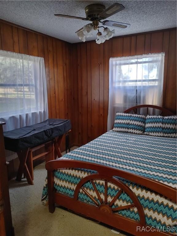 bedroom featuring multiple windows, wood walls, a textured ceiling, and carpet flooring