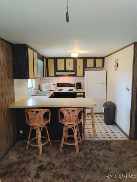 kitchen with white appliances, a sink, carpet, under cabinet range hood, and backsplash