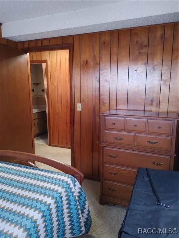 bedroom featuring wood walls, connected bathroom, and light colored carpet