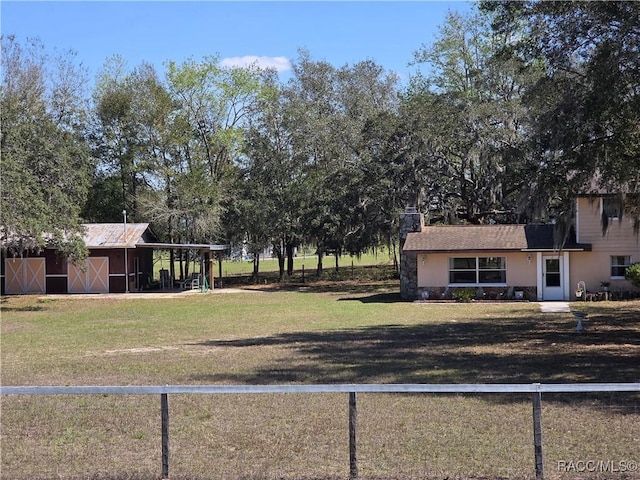 view of yard with a carport, an outbuilding, fence, and a barn