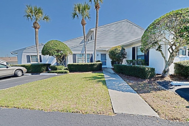 view of front of house featuring uncovered parking, a front lawn, and stucco siding