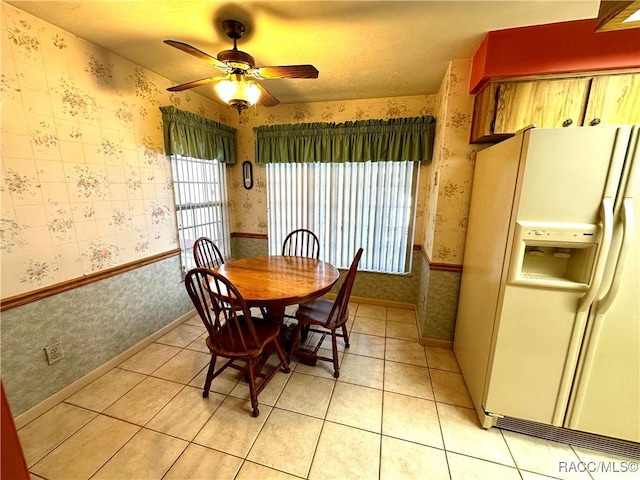 dining area with light tile patterned floors, a wainscoted wall, ceiling fan, and wallpapered walls