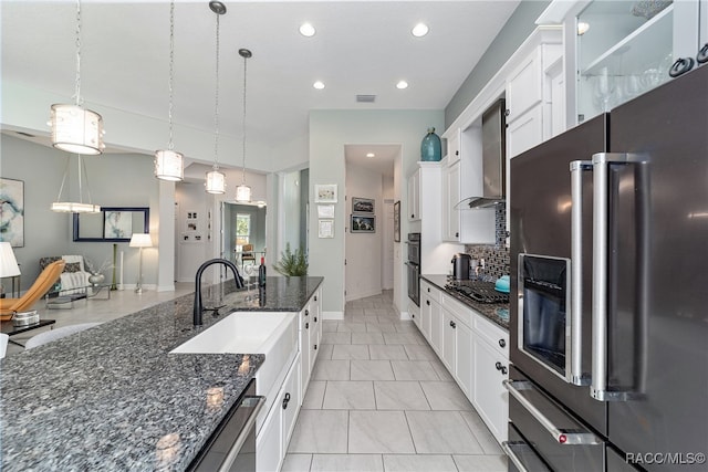 kitchen with white cabinets, decorative light fixtures, wall chimney range hood, and appliances with stainless steel finishes