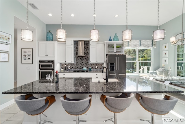 kitchen featuring a breakfast bar, wall chimney exhaust hood, hanging light fixtures, and appliances with stainless steel finishes