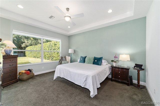 bedroom with dark colored carpet, a tray ceiling, and ceiling fan