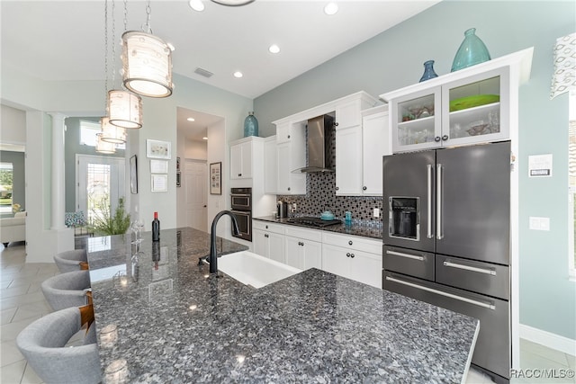 kitchen with sink, wall chimney range hood, decorative light fixtures, white cabinets, and appliances with stainless steel finishes