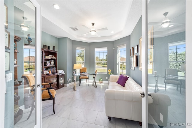 living room featuring a raised ceiling, ceiling fan, french doors, and a healthy amount of sunlight