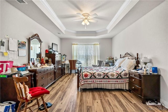 bedroom featuring a raised ceiling, visible vents, a ceiling fan, crown molding, and light wood-style flooring
