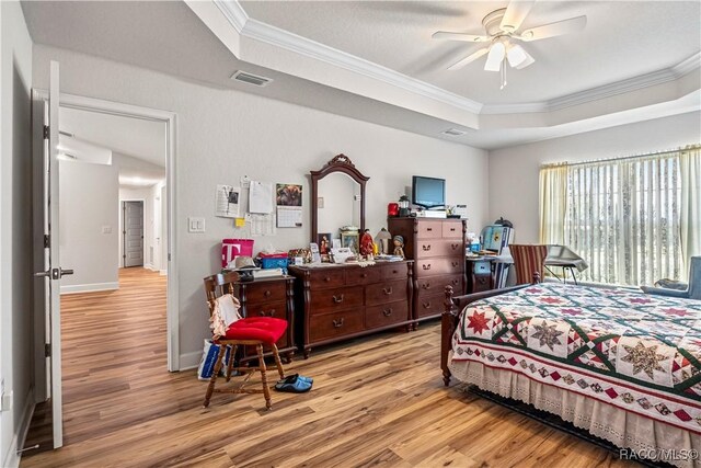 bedroom with light wood-style flooring, visible vents, a raised ceiling, and crown molding