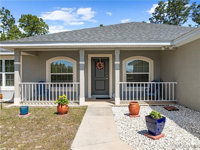 doorway to property featuring a porch, a shingled roof, and stucco siding