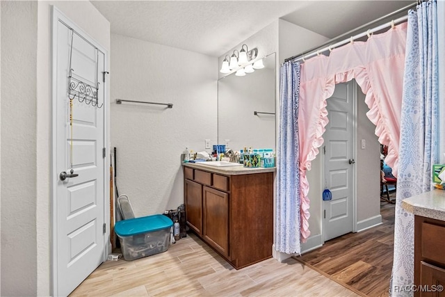 full bath featuring wood finished floors, a textured ceiling, vanity, and a textured wall
