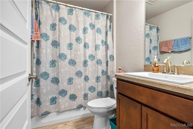 bathroom featuring shower / bath combo, toilet, wood finished floors, a textured wall, and vanity