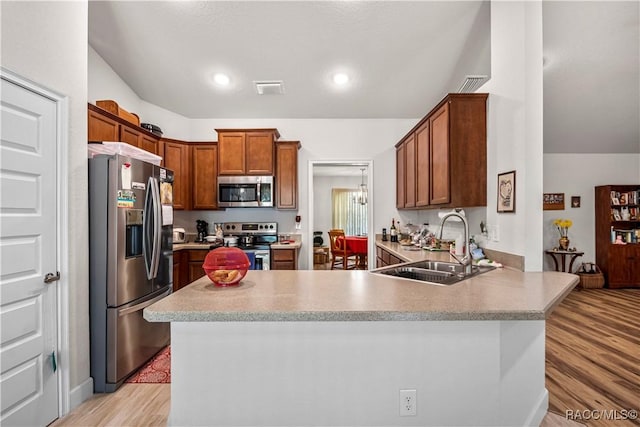 kitchen with a sink, light countertops, stainless steel appliances, light wood-style flooring, and a peninsula