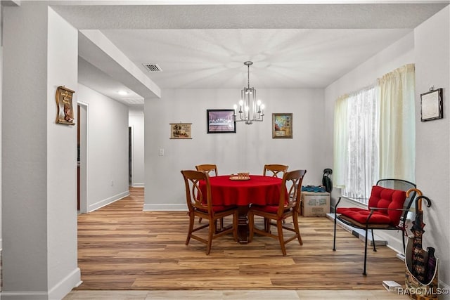 dining room with baseboards, wood finished floors, visible vents, and an inviting chandelier