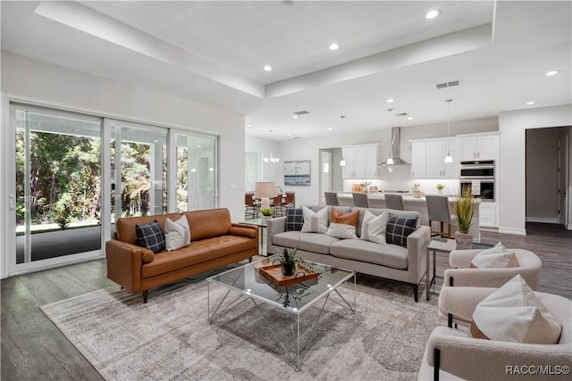 living room with a chandelier, wood-type flooring, and a raised ceiling