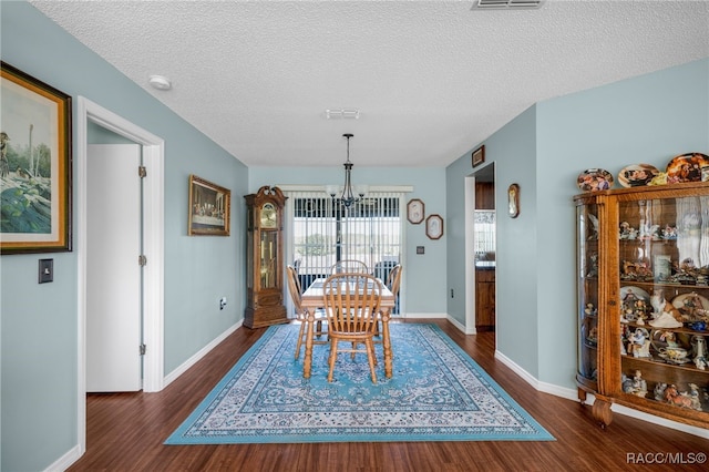 dining space with dark wood-style floors, a textured ceiling, a notable chandelier, and baseboards