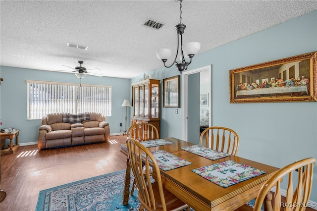 dining room featuring ceiling fan with notable chandelier, visible vents, a textured ceiling, and wood finished floors