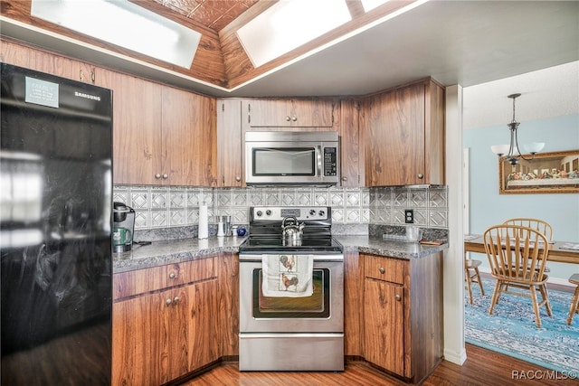 kitchen with light wood-style flooring, stainless steel appliances, backsplash, brown cabinets, and dark countertops