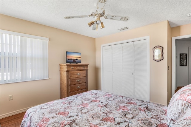 bedroom with a closet, visible vents, a textured ceiling, and wood finished floors