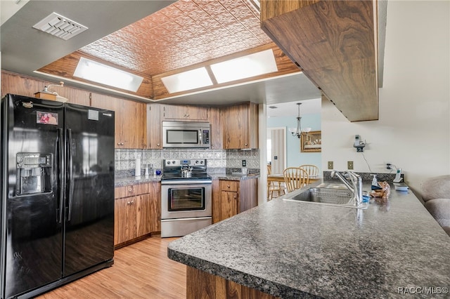 kitchen featuring stainless steel appliances, a sink, visible vents, backsplash, and brown cabinets