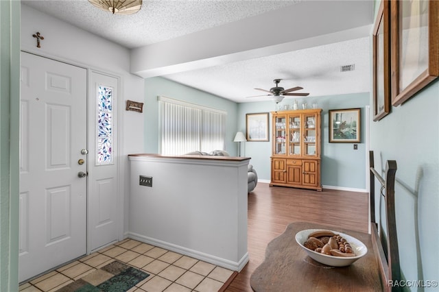 foyer featuring visible vents, light wood-style floors, ceiling fan, a textured ceiling, and baseboards