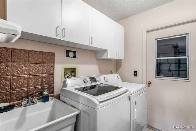 laundry area featuring a textured ceiling, separate washer and dryer, a sink, and cabinet space