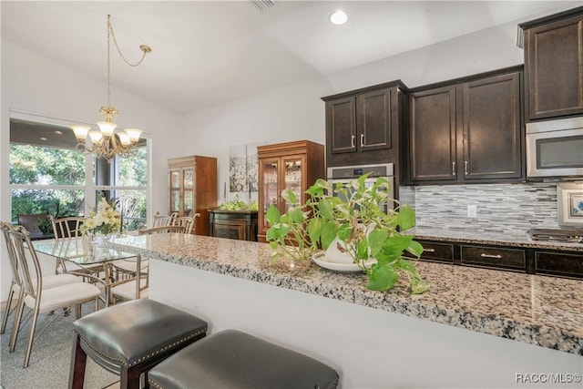 kitchen featuring lofted ceiling, dark brown cabinets, pendant lighting, light stone countertops, and decorative backsplash