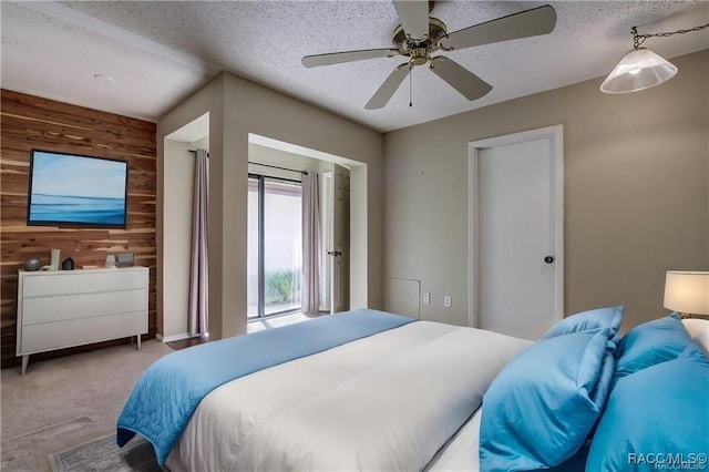 bedroom featuring wooden walls, ceiling fan, access to outside, light colored carpet, and a textured ceiling