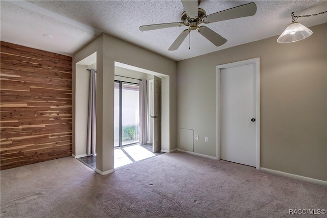 empty room with carpet, ceiling fan, wood walls, and a textured ceiling