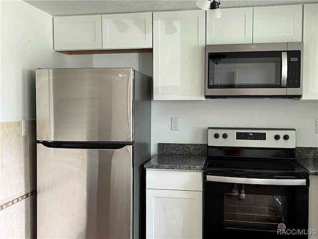 kitchen featuring dark stone countertops, white cabinets, and stainless steel appliances