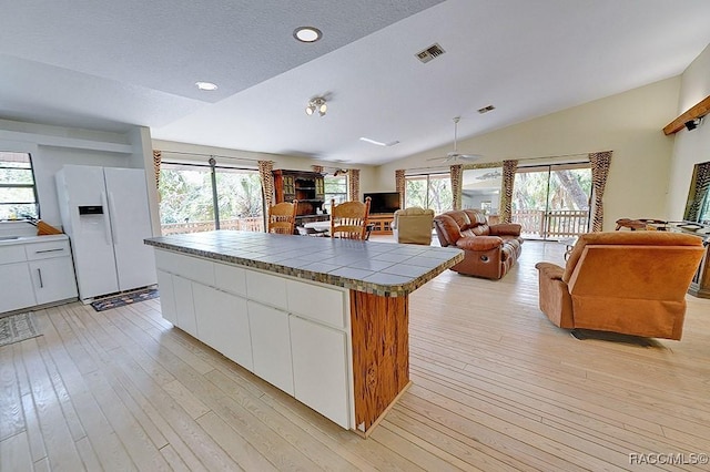 kitchen featuring lofted ceiling, light wood-type flooring, white fridge with ice dispenser, and white cabinets