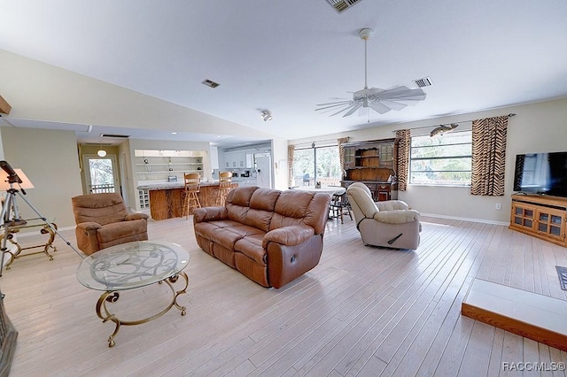 living room featuring built in shelves, light wood finished floors, lofted ceiling, visible vents, and a ceiling fan