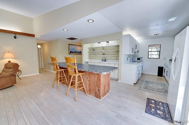 kitchen featuring white appliances, a breakfast bar area, visible vents, and light wood-style floors