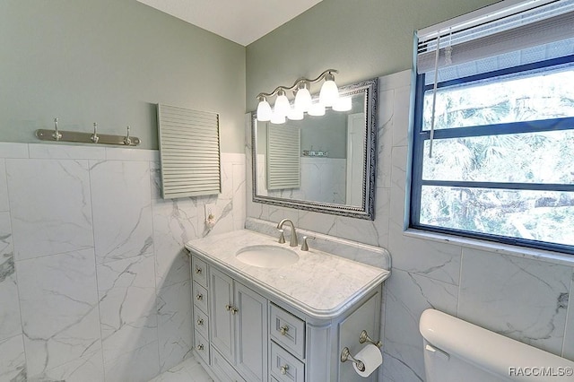 bathroom with toilet, radiator, marble finish floor, vanity, and tile walls