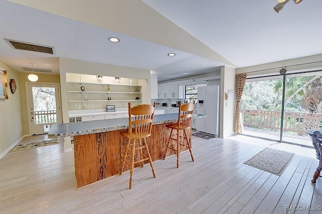 kitchen with white refrigerator with ice dispenser, visible vents, tile counters, light wood-style flooring, and a kitchen breakfast bar