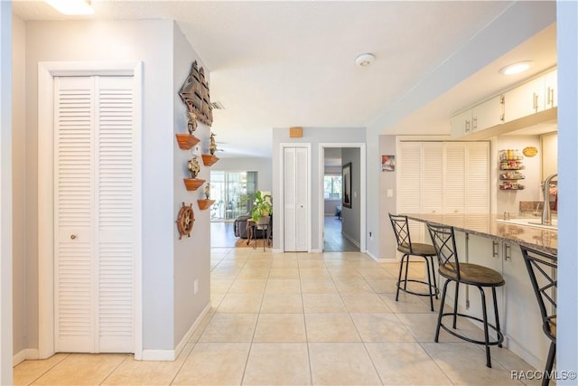 kitchen with light tile patterned flooring, stone countertops, a kitchen bar, and white cabinets