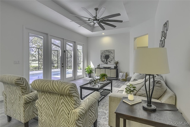 living room with ceiling fan, light hardwood / wood-style flooring, a tray ceiling, and french doors