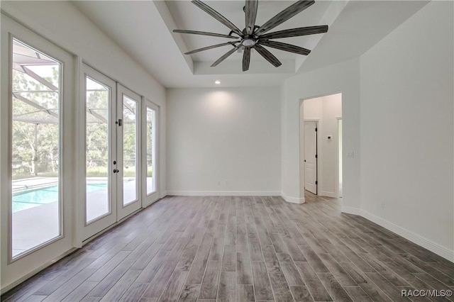 empty room with french doors, a tray ceiling, light hardwood / wood-style flooring, and ceiling fan