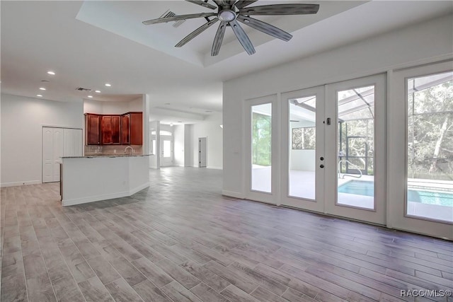 unfurnished living room with a tray ceiling, ceiling fan, french doors, and light wood-type flooring