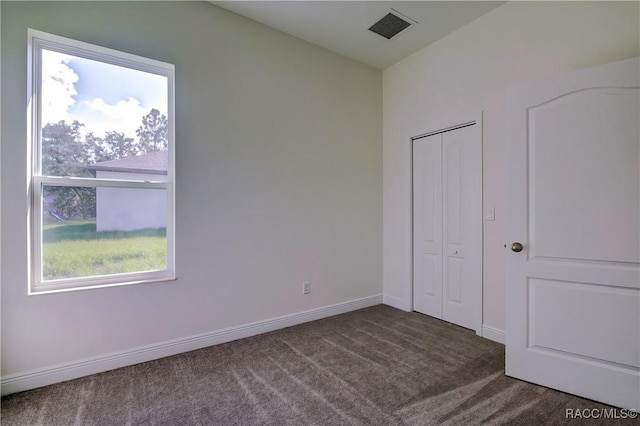 unfurnished bedroom with dark colored carpet and a closet