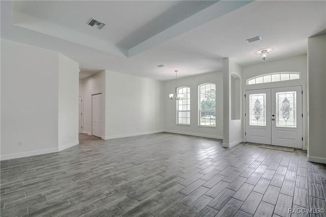 foyer featuring a raised ceiling, french doors, and a chandelier