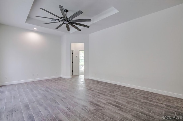 empty room featuring ceiling fan, a raised ceiling, and light wood-type flooring