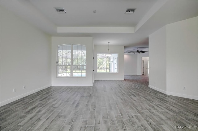 unfurnished living room with a raised ceiling, ceiling fan, and light hardwood / wood-style floors