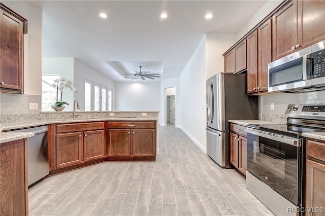 kitchen featuring ceiling fan, sink, light stone countertops, appliances with stainless steel finishes, and light wood-type flooring