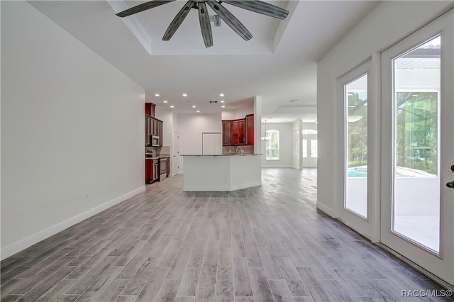 unfurnished living room featuring light wood-type flooring, a raised ceiling, and ceiling fan