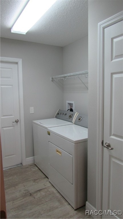 washroom with washing machine and dryer, light hardwood / wood-style floors, and a textured ceiling